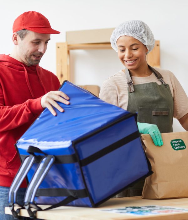 Waist up portrait of two workers smiling while packaging orders at food delivery service, copy space