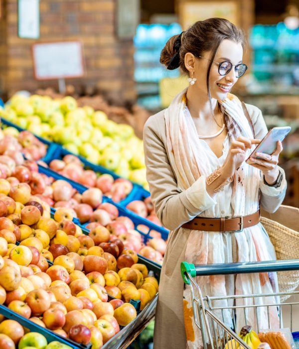 Young woman looking on the shopping list using smartphone while shopping food in the supermarket